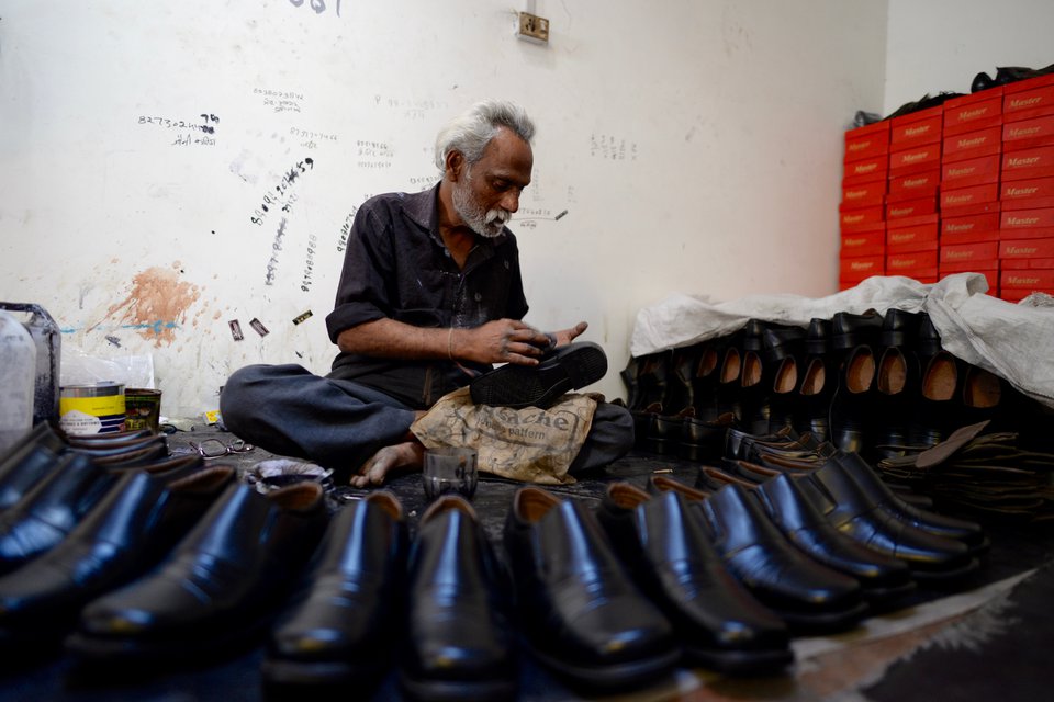 Arbeiter umringt von Schuhen, die er gerade poliert